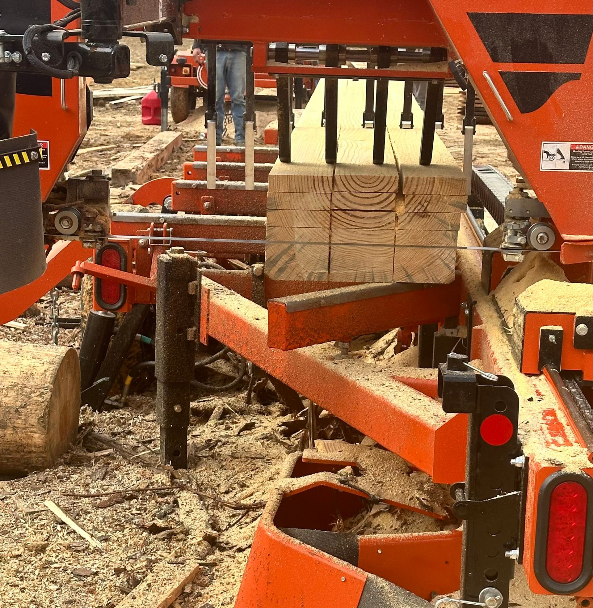 A wood saw cutting a wooden beam into square pieces; sawdust is visible.
