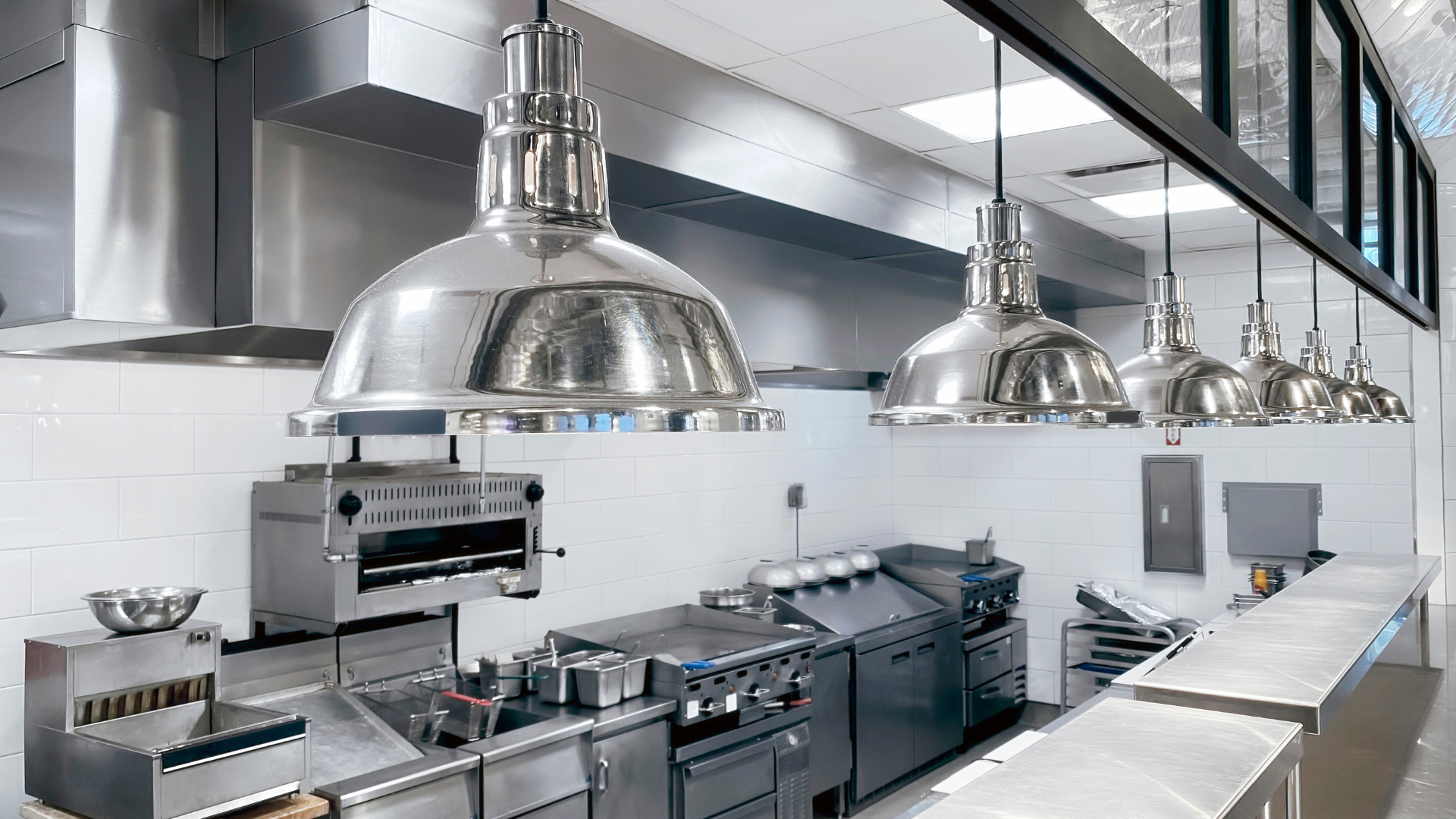 A kitchen with a lot of stainless steel appliances and lamps hanging from the ceiling.