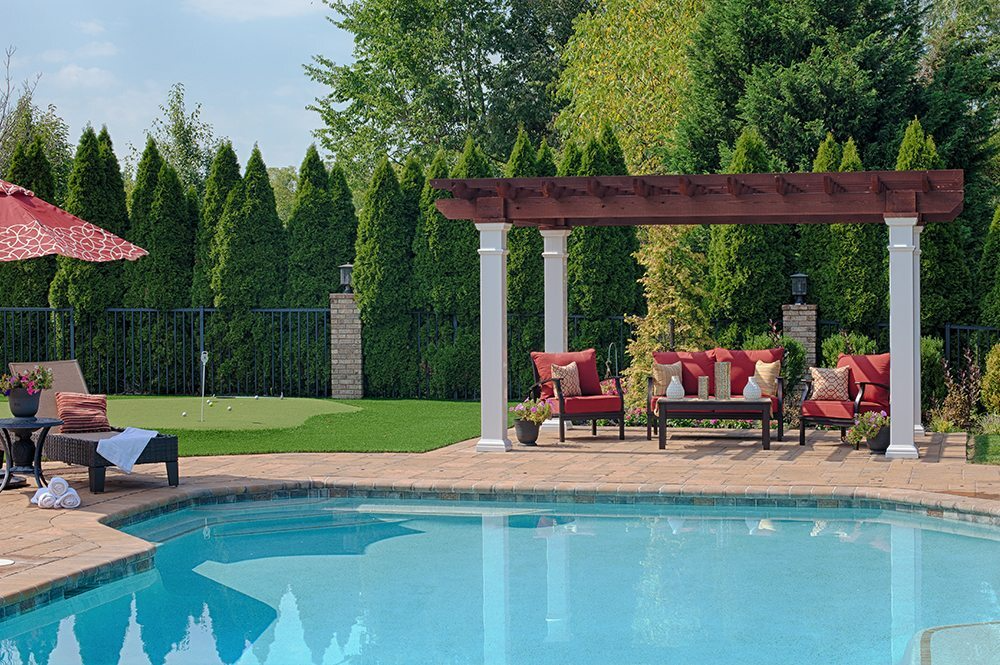 Backyard pool with lounge chairs and a pergola seating area on a sunny day