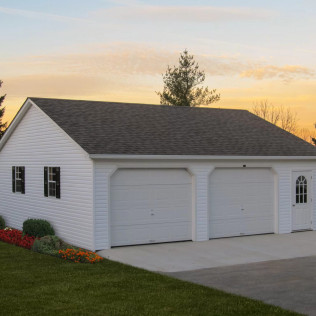 White two-car garage with double doors and a driveway at sunset, surrounded by grass and flowers