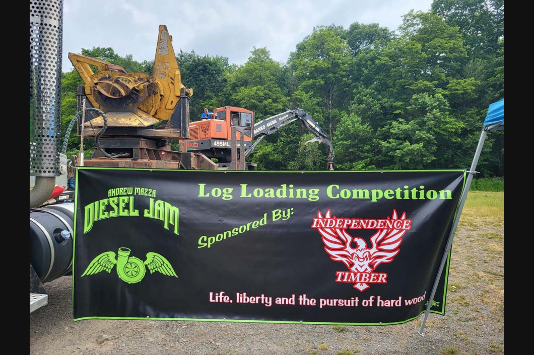 Banner for a log loading competition with a yellow logging machine outdoors in a forested area