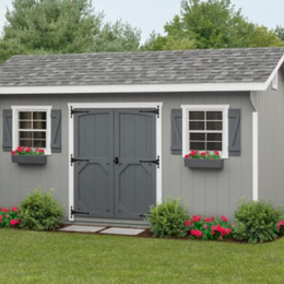 Gray garden shed with double doors, white trim, flower boxes, and red flowers in front of a lawn and trees