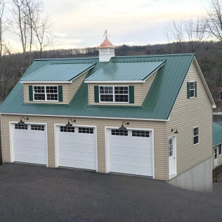 Beige house with green roof and three white garage doors, viewed from the driveway.