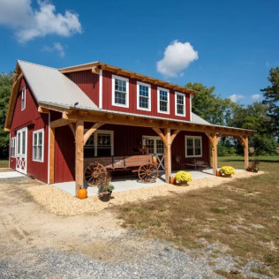 Red barn-style house with a wraparound porch, white trim, and a white metal roof under a blue sky