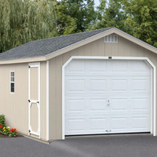 Beige shed with white garage door and asphalt driveway, bordered by trees and flowers