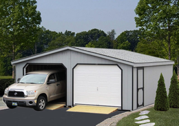 Light gray detached garage with a silver van parked inside, surrounded by green trees.