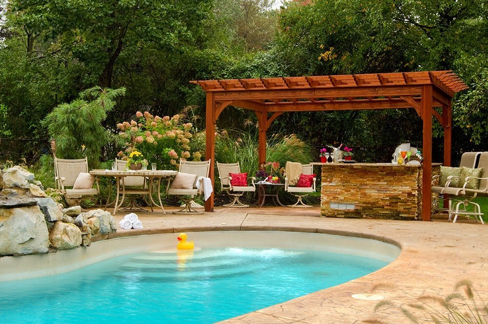 Backyard pool with stone patio, wooden pergola, lounge chairs, and lush greenery