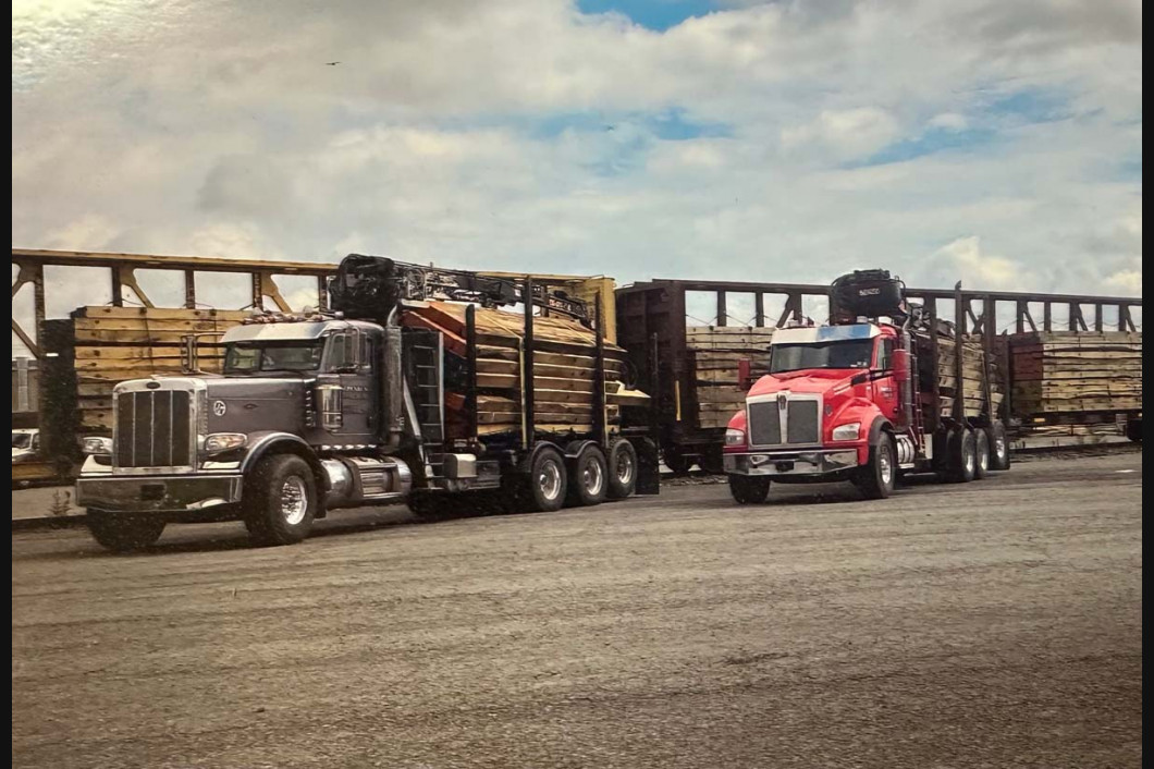 Two semi trucks parked on a dirt lot, one silver and one red, with trailers behind them under a cloudy sky