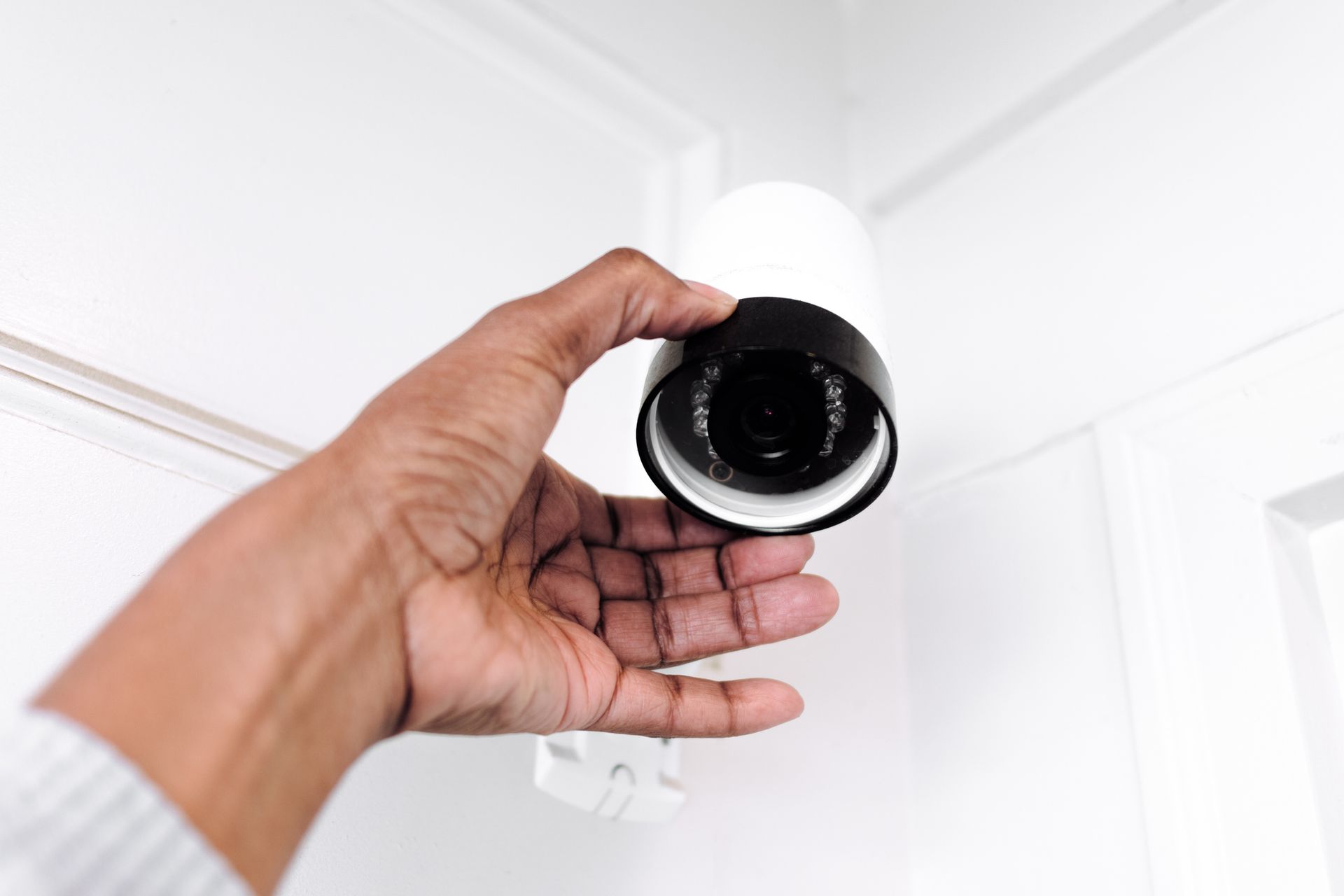 Close-up of a hand adjusting a security camera placed in the corner of a ceiling. Close-up of a hand adjusting a security camera placed in the corner of a ceiling.