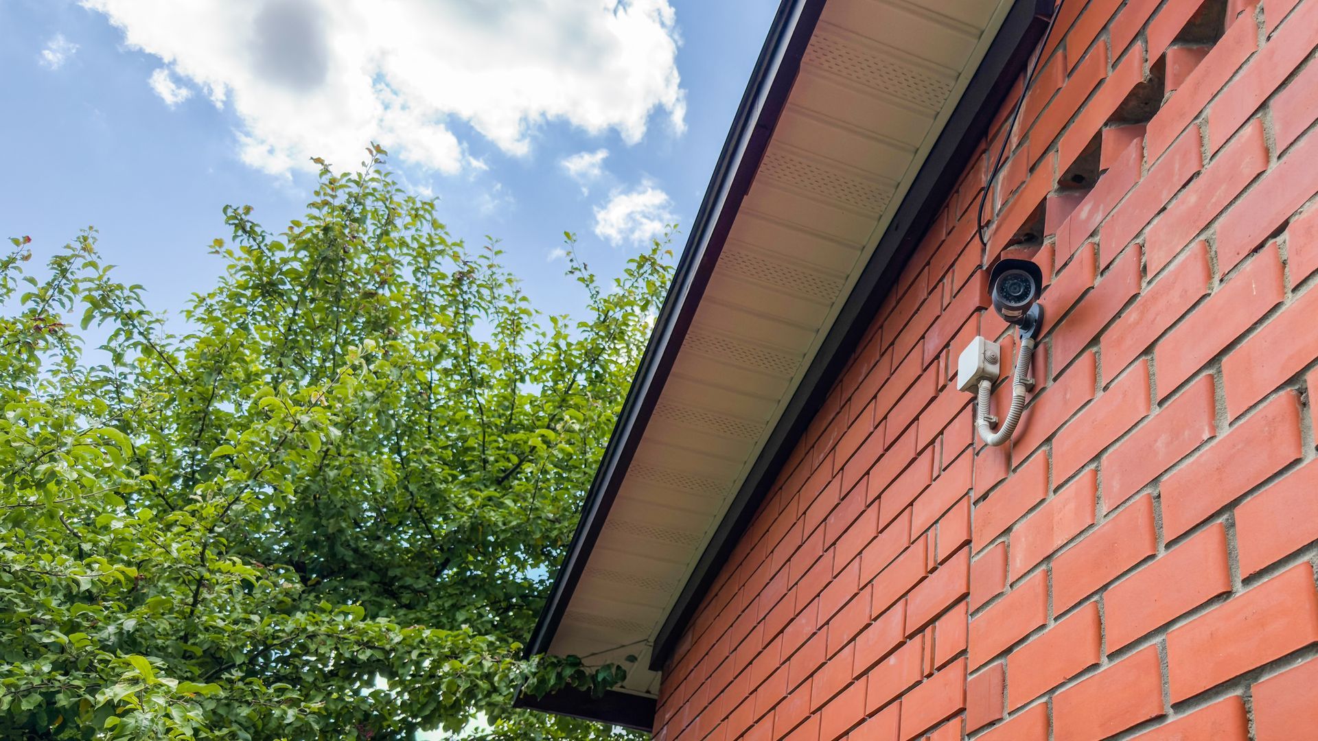 Red brick house with roof camera under blue sky and leafy tree. Red brick house with roof camera under blue sky and leafy tree.