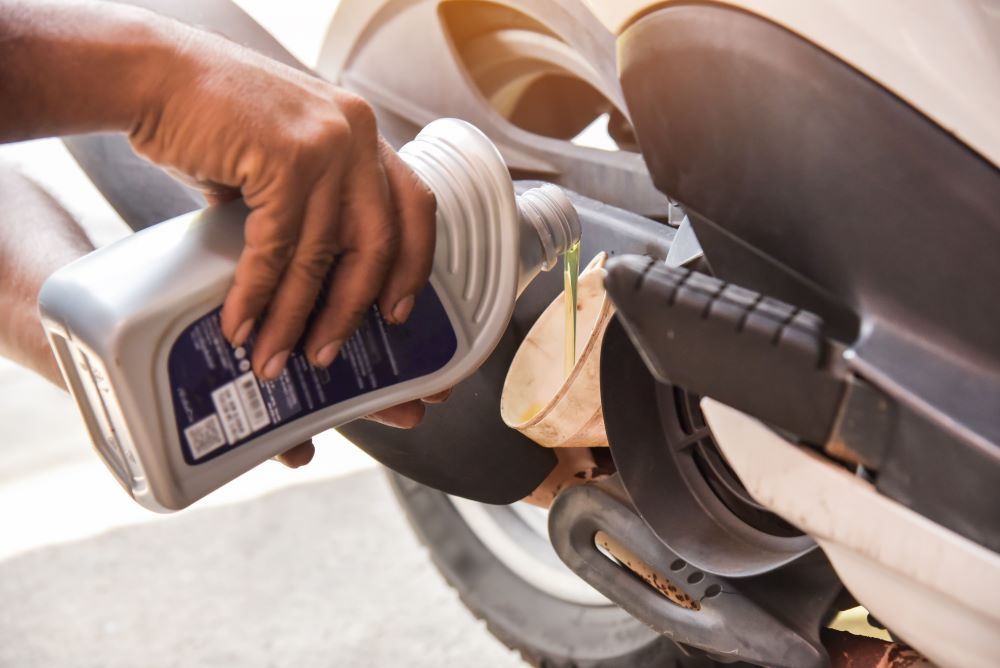 Person Pouring Oil from A Bottle Into a Scooter Engine — Haigh Truck & 4WD Repairs In Orange, NSW