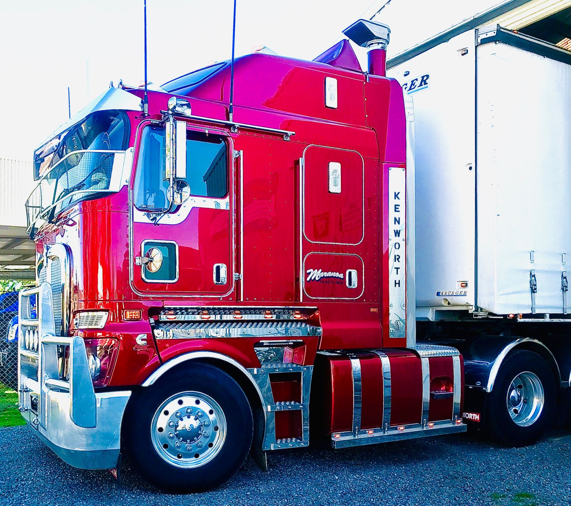 Red semi-truck with chrome details, parked on gravel, hauling a white trailer.