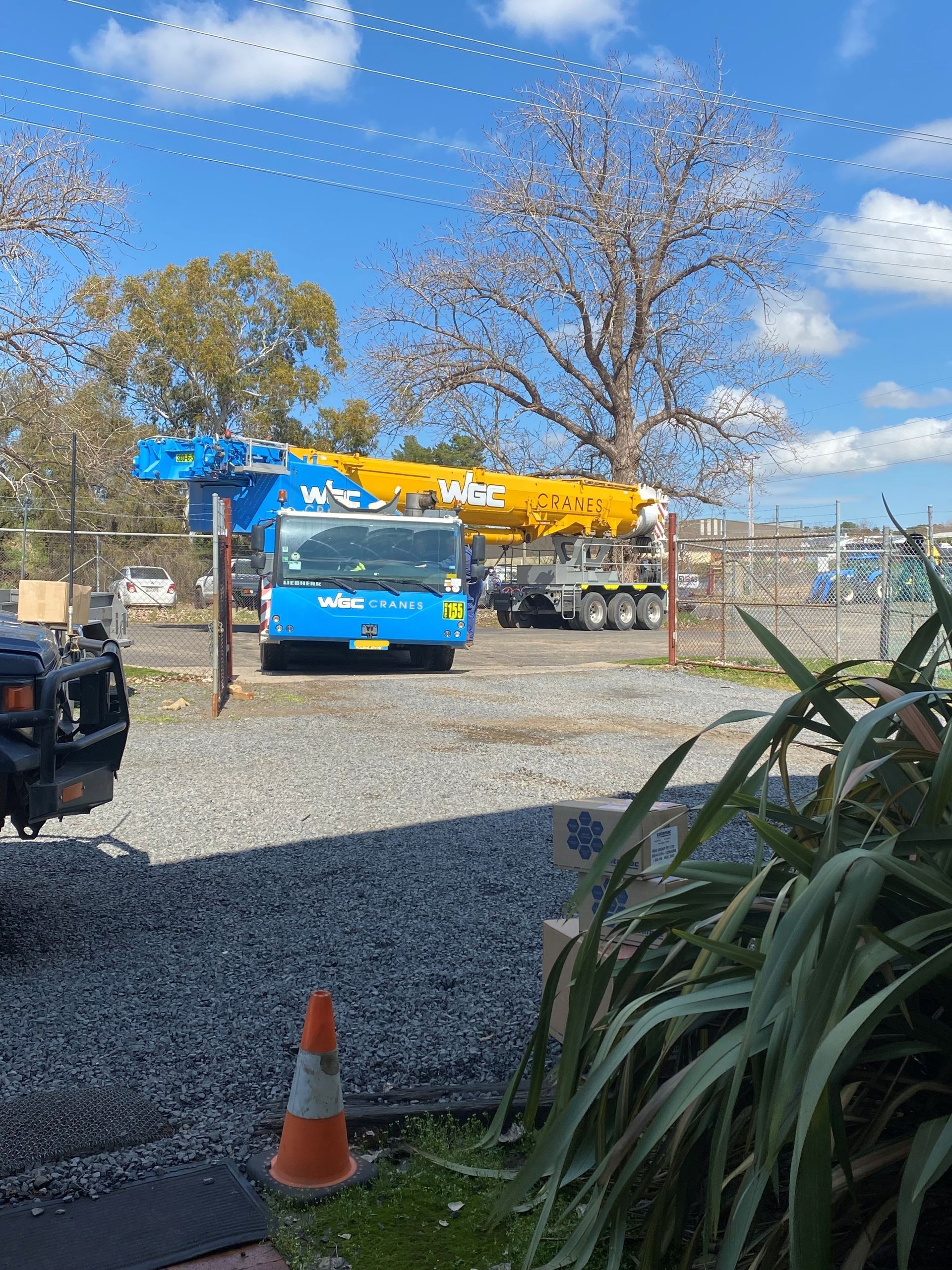 Blue crane truck parked on gravel lot under a sunny blue sky.
