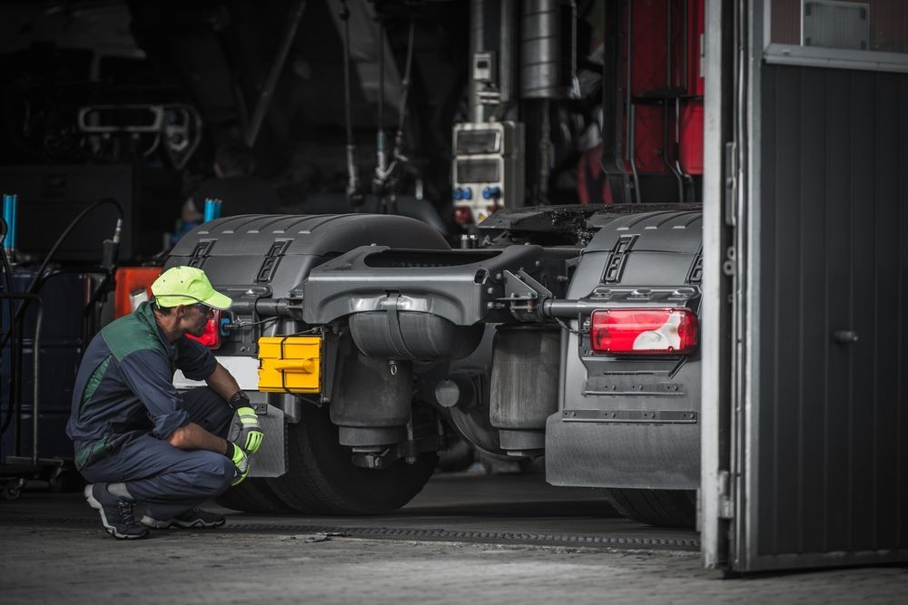 Mechanic in Safety Gear Inspecting a Truck's Undercarriage in A Garage — Haigh Truck & 4WD Repairs In Orange, NSW