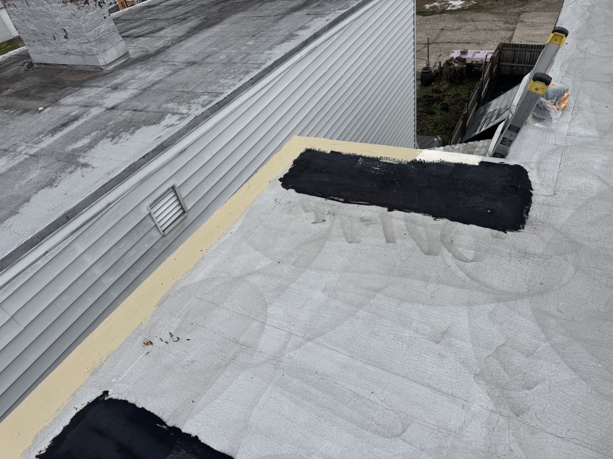 Roller applying tan silicone coating along flat roof wall flashing