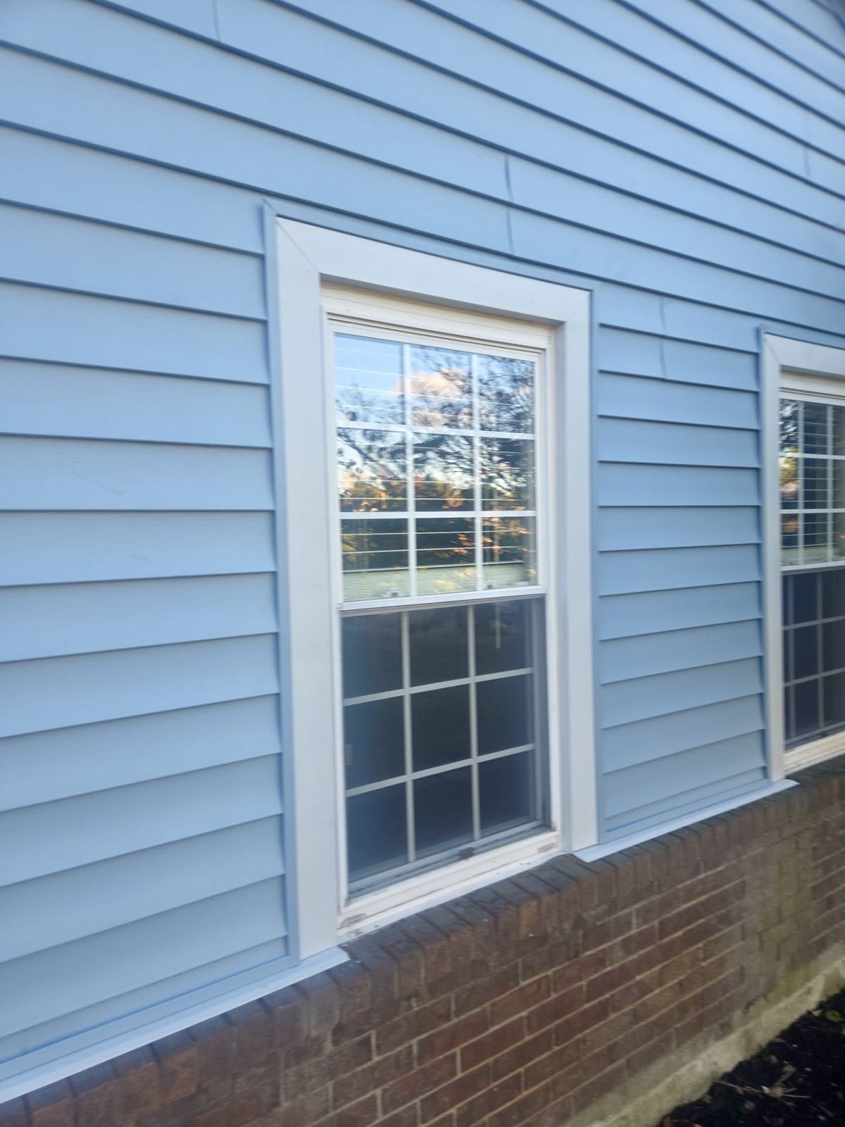 Finished blue horizontal vinyl siding with white window trim above a brick foundation wall