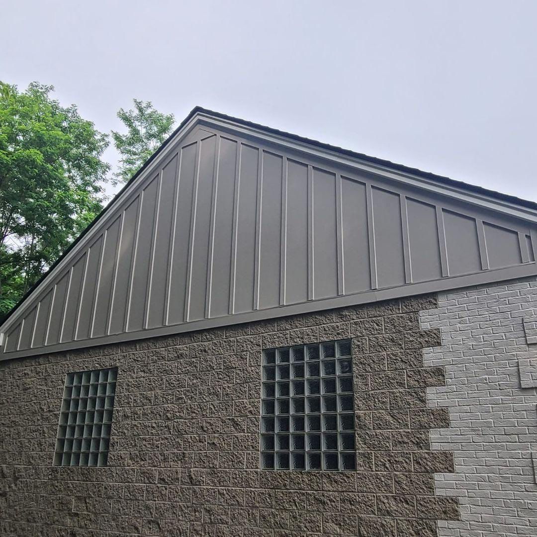 Gray-brown board and batten gable siding above a split-face block wall with glass block windows