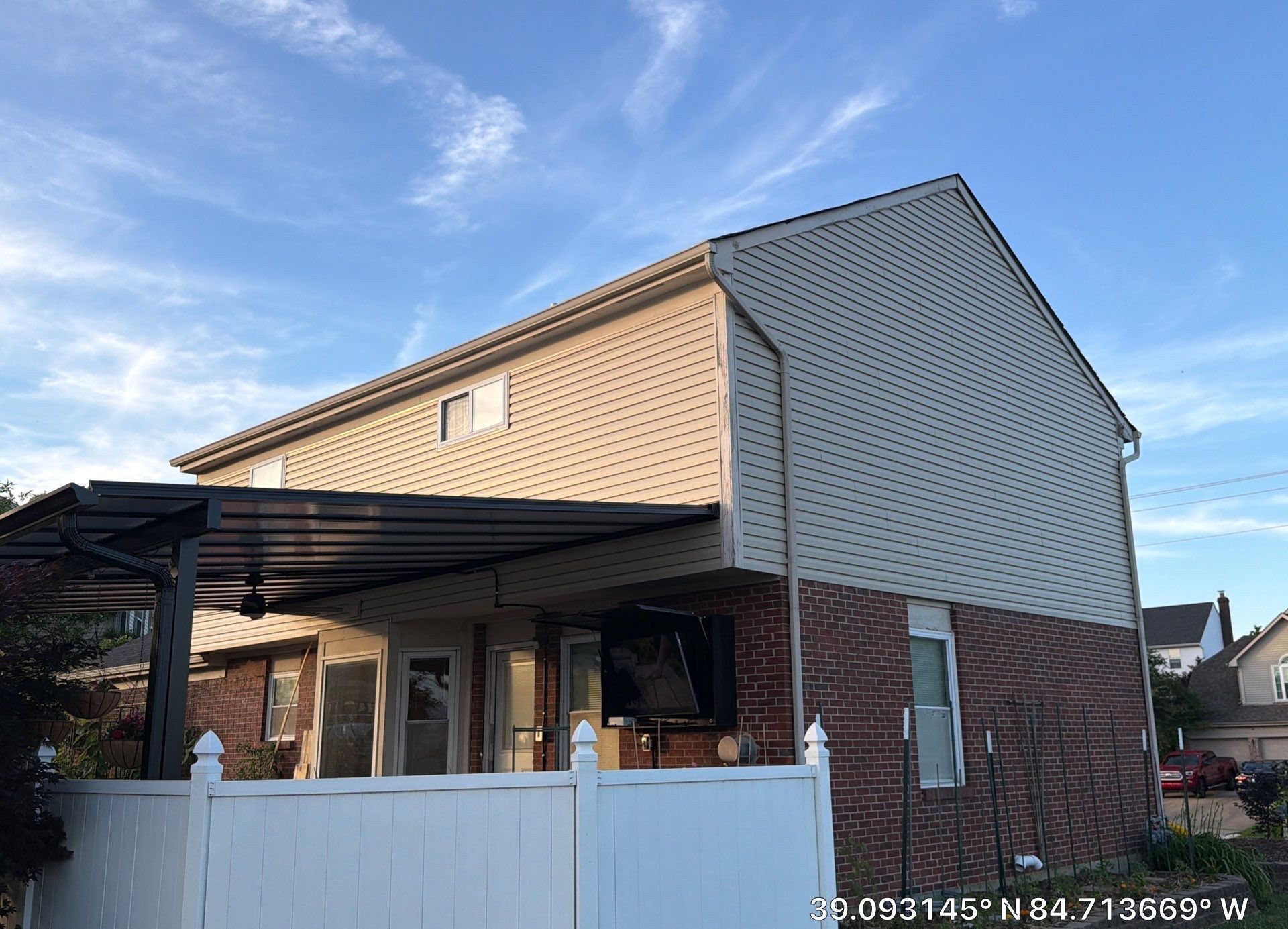Brick home with light upper siding and a covered patio with ceiling fan