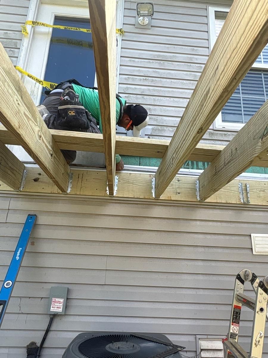 Fortress Solutions crew member installing pressure-treated deck joists with metal joist hangers on the ledger board