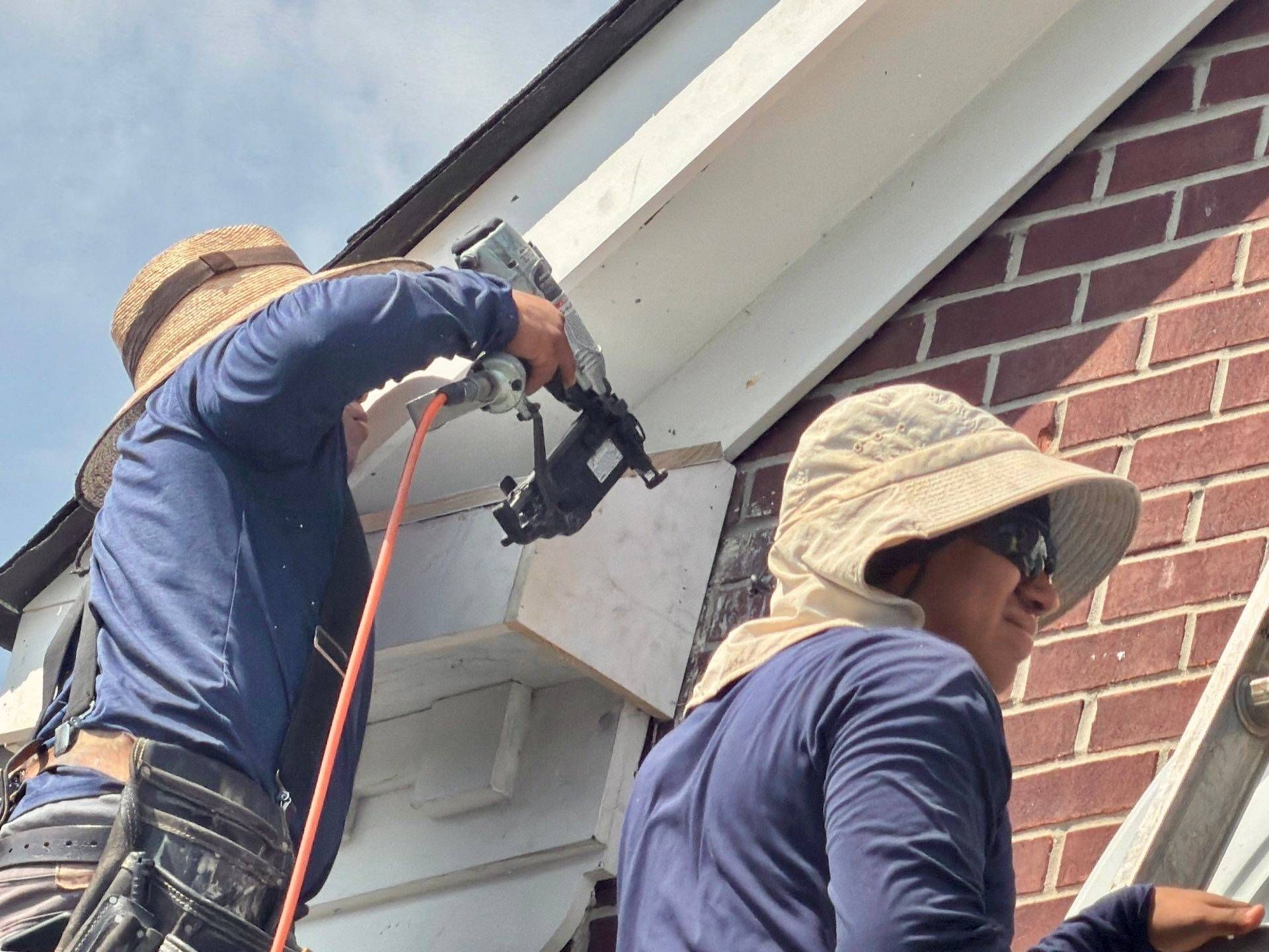 Two Fortress Solutions crew members nailing new white fascia trim and a gable return on a brick home
