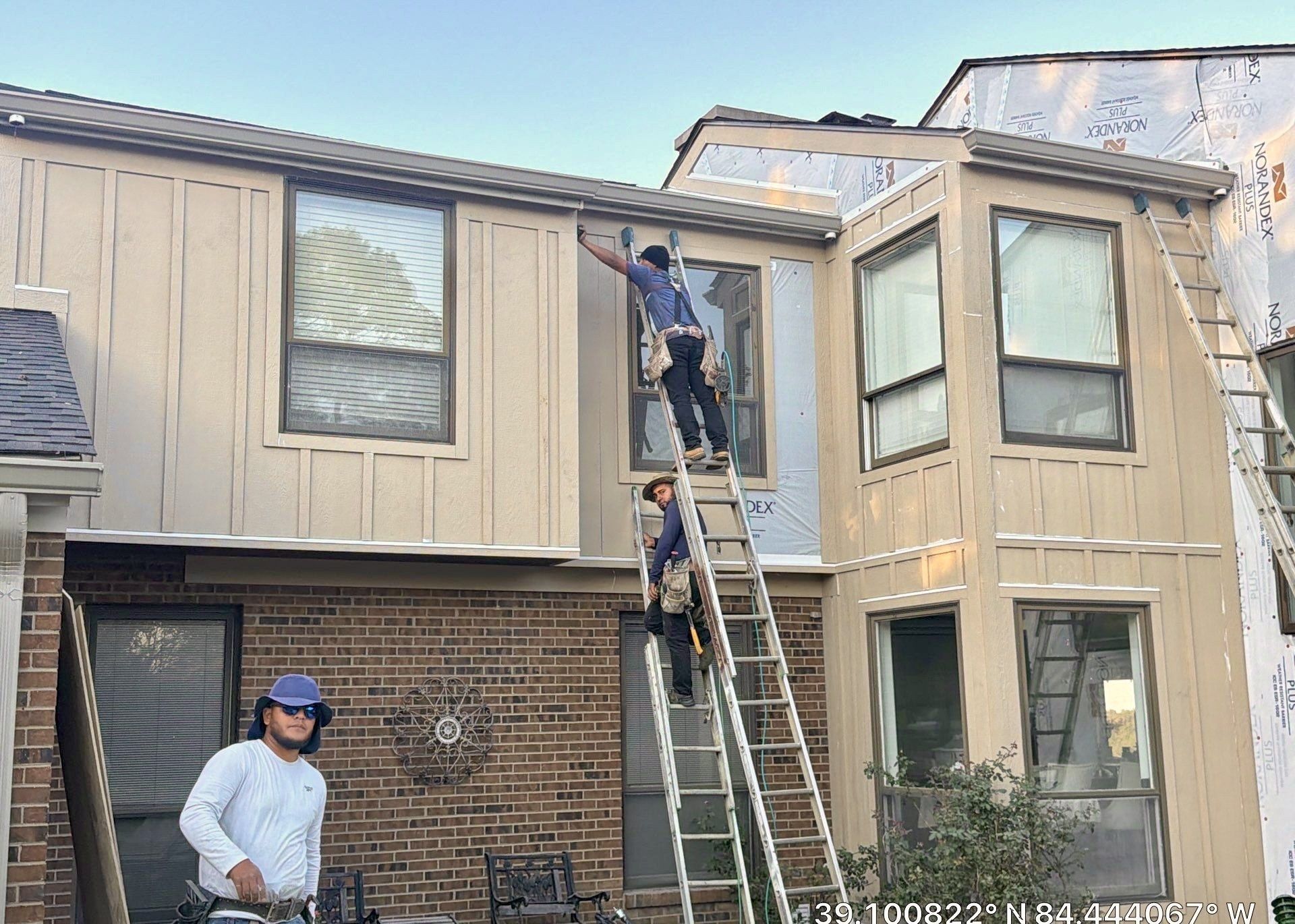Crew on ladders installing board and batten siding on a brick home with house wrap still showing