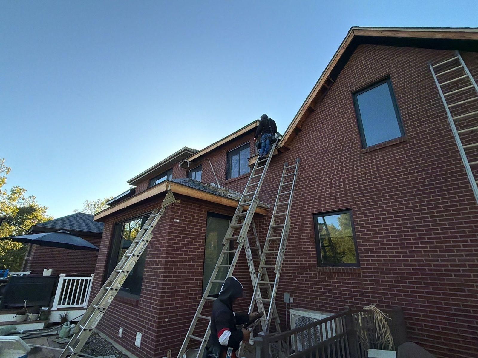 Crew members on extension ladders repairing fascia on the rear of a two-story red brick home