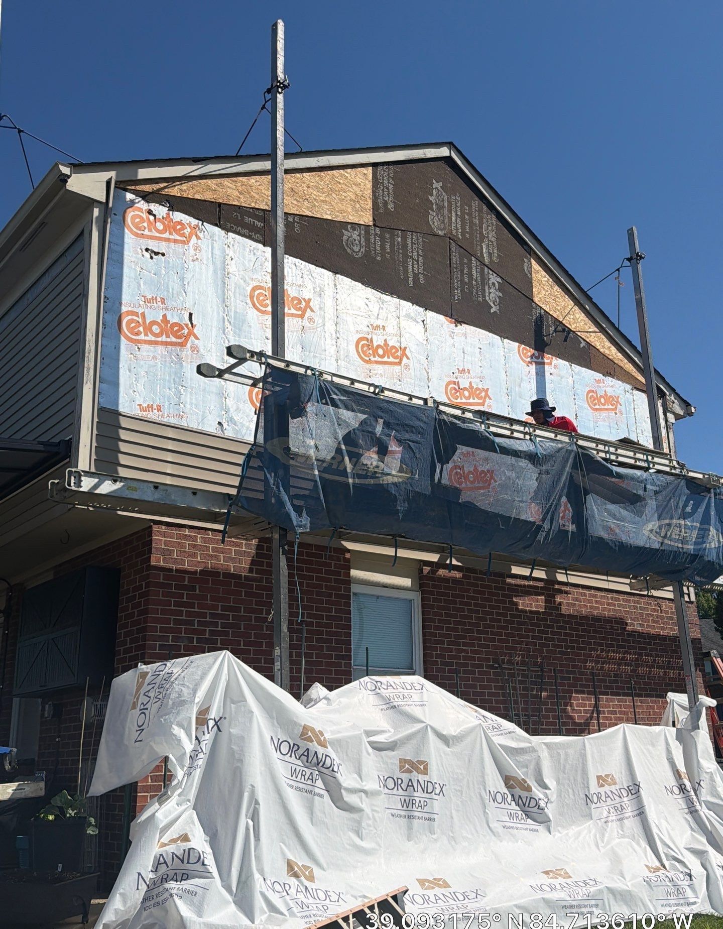 Crew member on scaffolding installing upper siding over sheathing on a brick home