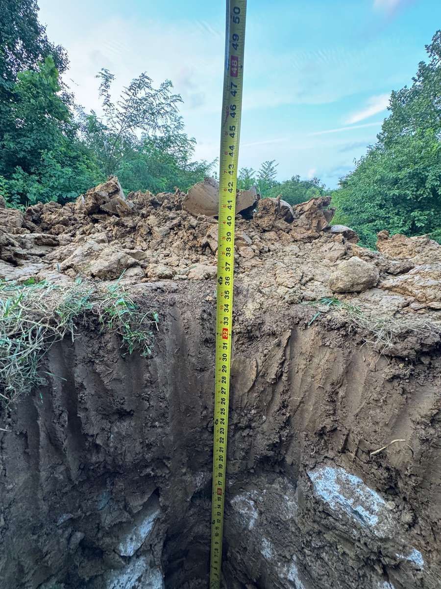 Tape measure in a dug deck footing hole showing about 42 inches deep, with gravel at the bottom
