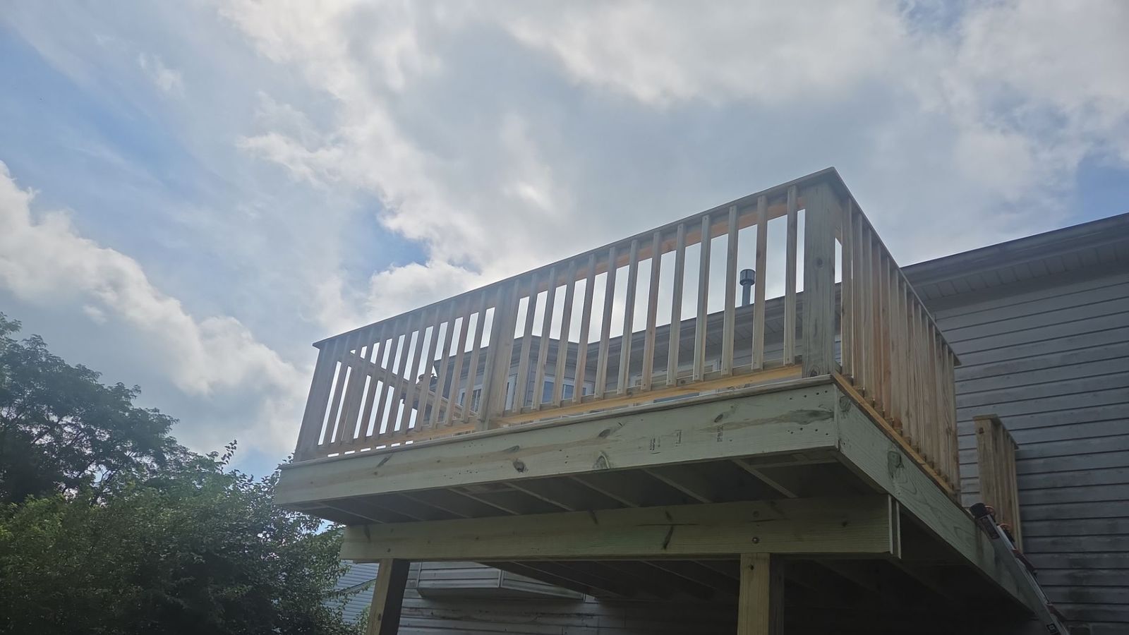 Elevated pressure-treated deck seen from below, showing the beams, posts, joists and railing against a vinyl-sided home