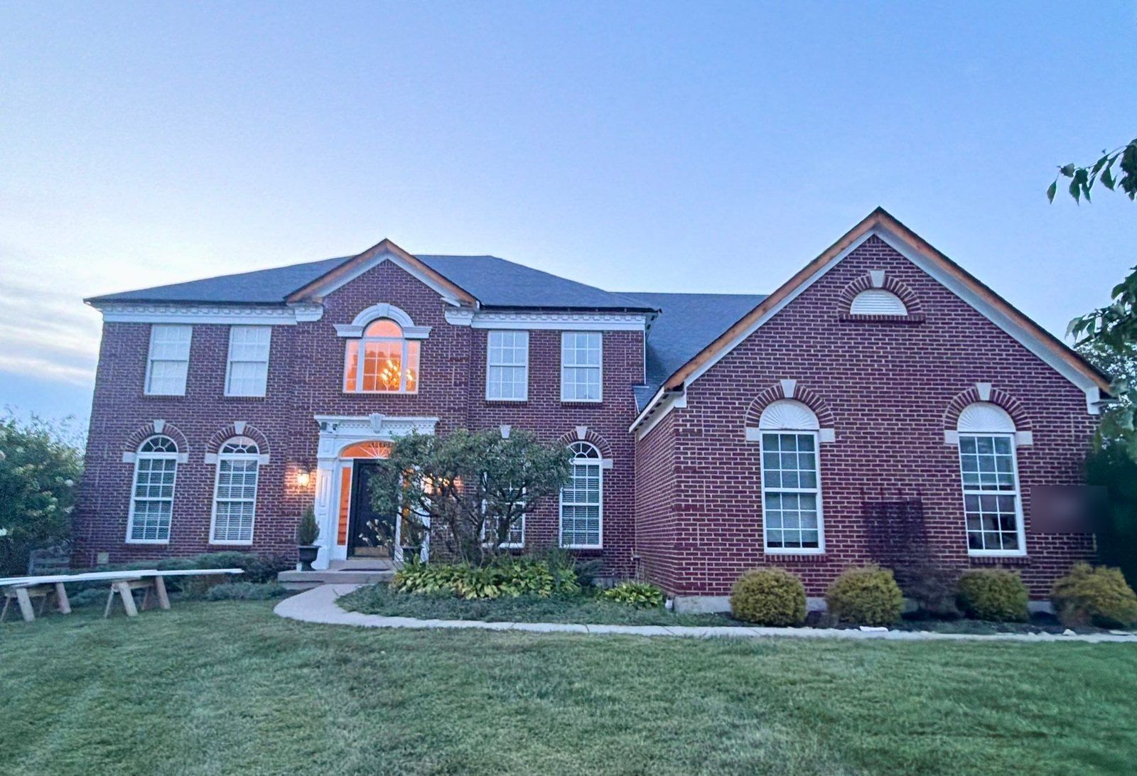 Fascia repair in progress on the front of a red brick colonial at dusk