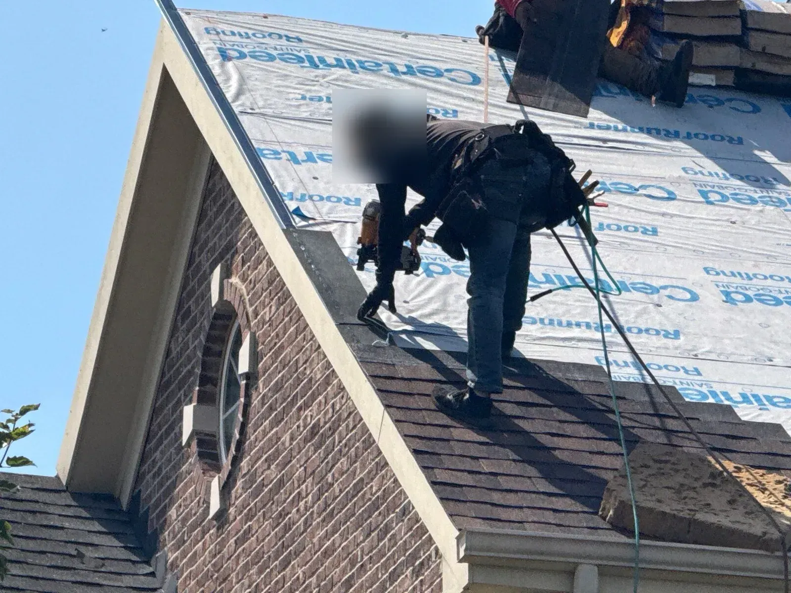 Roofer nailing new shingles at the gable edge over synthetic underlayment