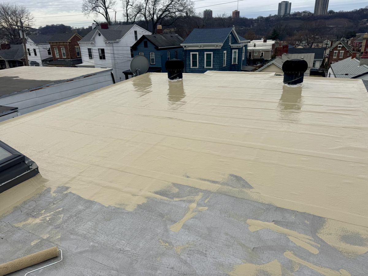 Tan CertainTeed Smartcoat 450 silicone coating partly applied over a cleaned flat roof