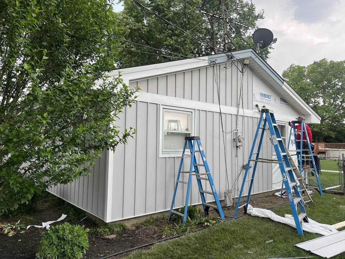Gray board and batten siding going up on a detached garage, with ladders and a crew member at work