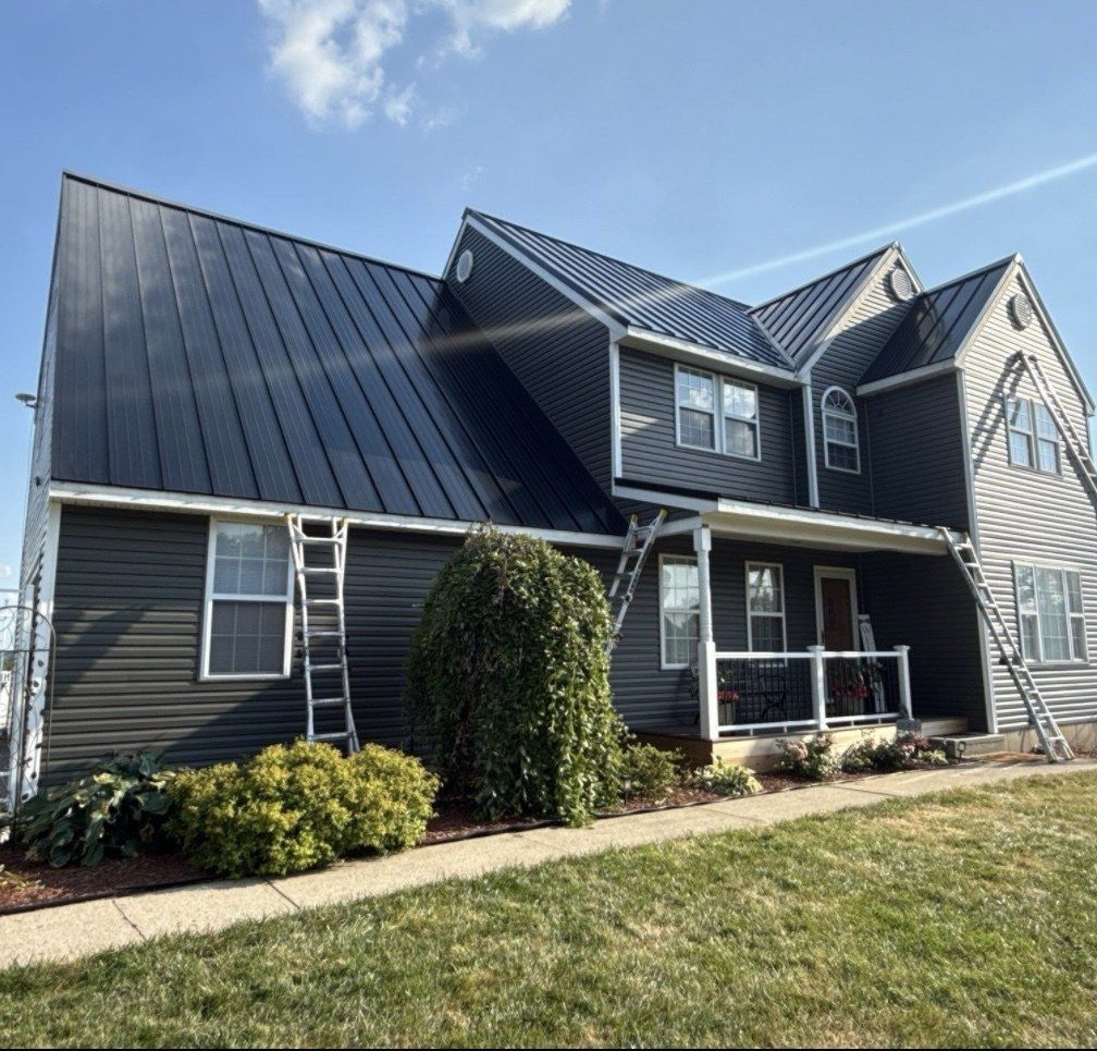 Two-story home in gray lap siding with a black metal roof and ladders on the front