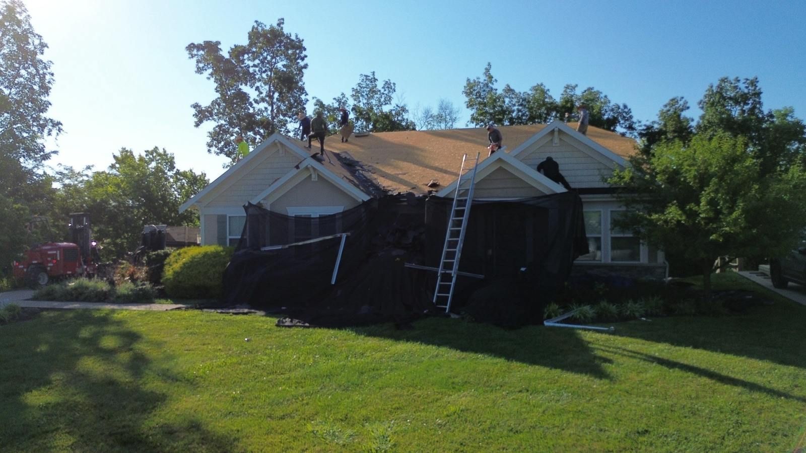 Roofers tearing off an old roof in Independence, KY with tarps protecting the shrubs and landscaping