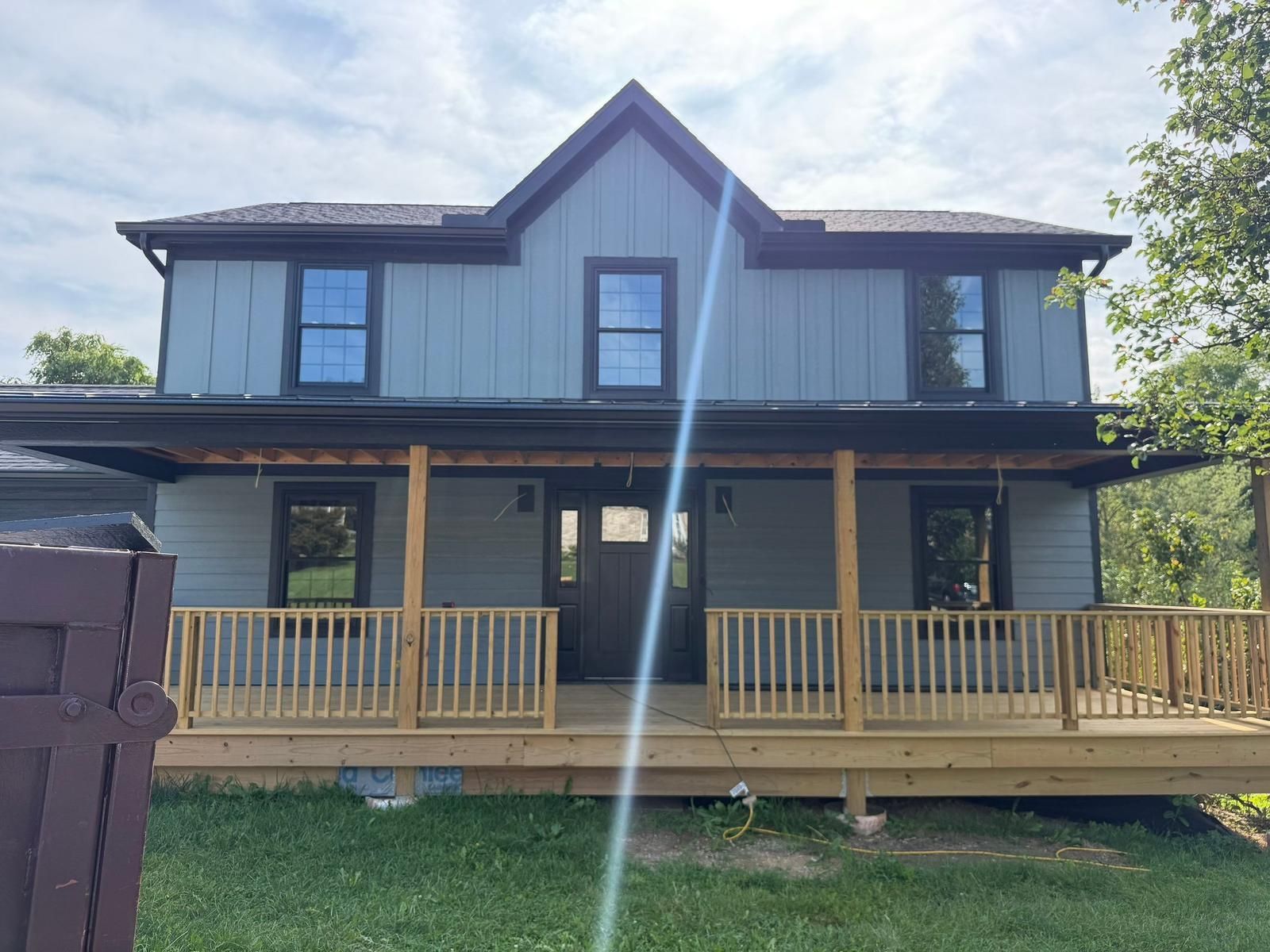 Two-story farmhouse finished in light blue board and batten and lap siding, with dark windows and a front porch