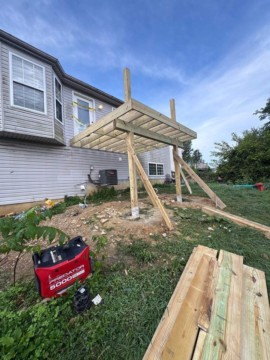 Pressure-treated wood deck frame on posts with diagonal bracing, being built off the back of a vinyl-sided home