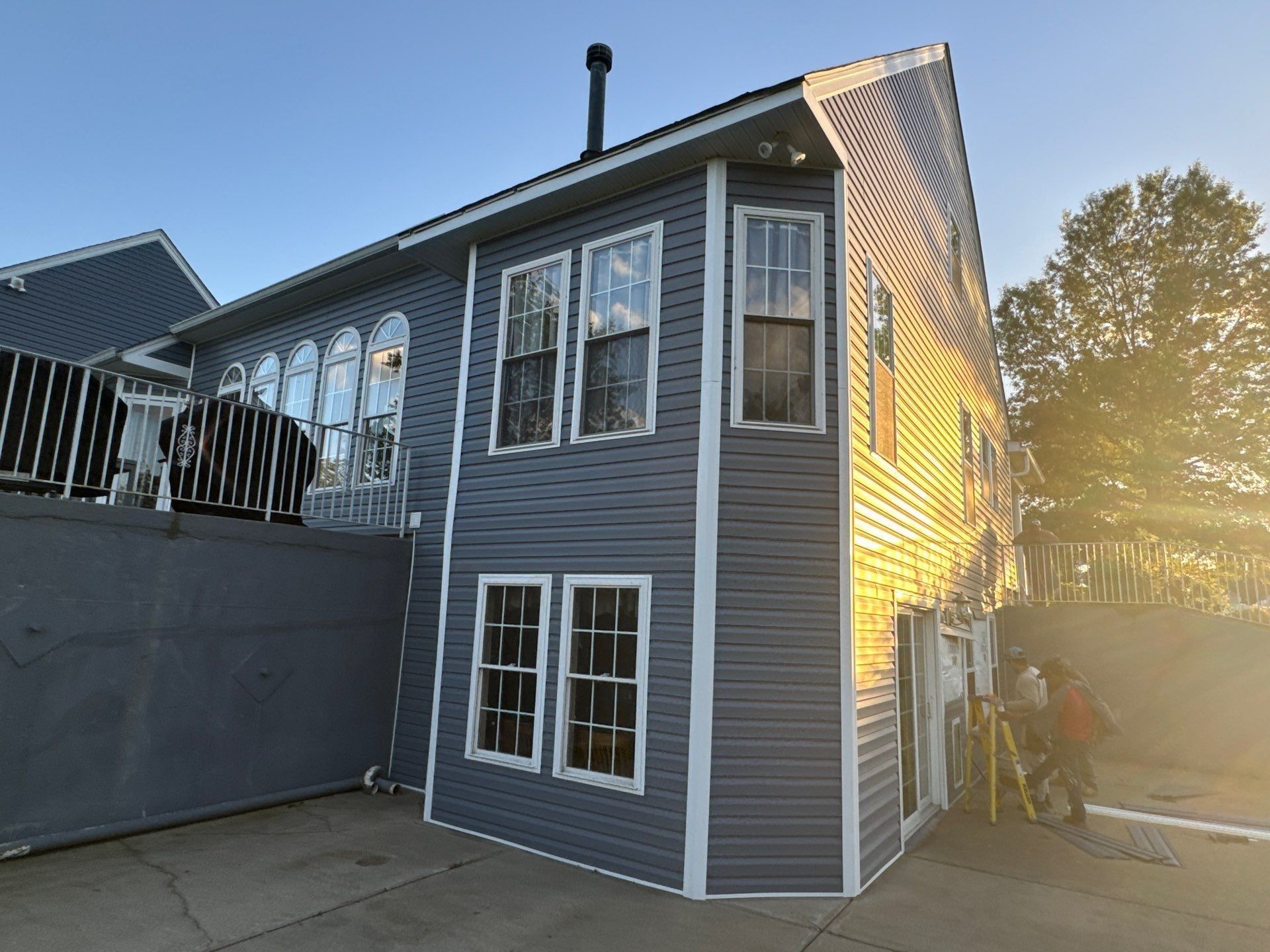 Slate blue lap siding going up on a multi-story home at golden hour, with crew on a ladder by the patio