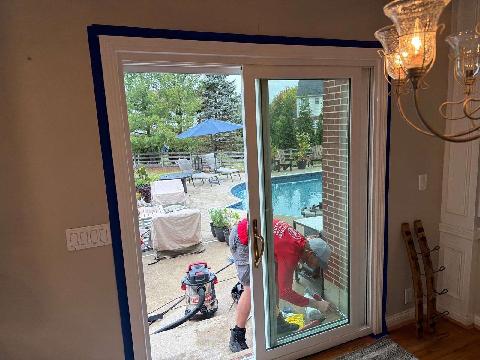 Fortress Solutions installer sealing the sill of a new white sliding patio door, viewed from inside the home