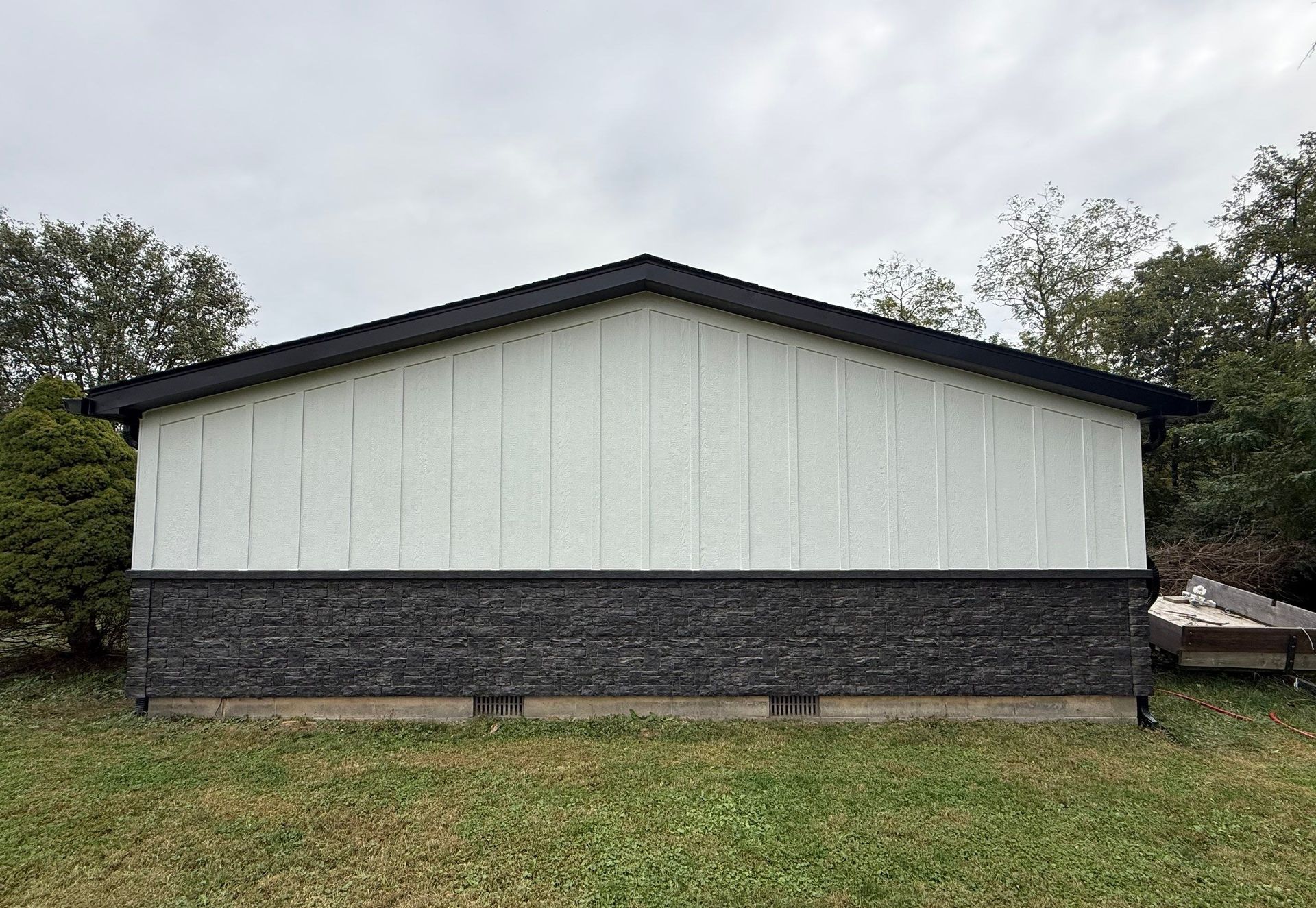 White board and batten gable siding above dark stone veneer on a garage or home, with black trim