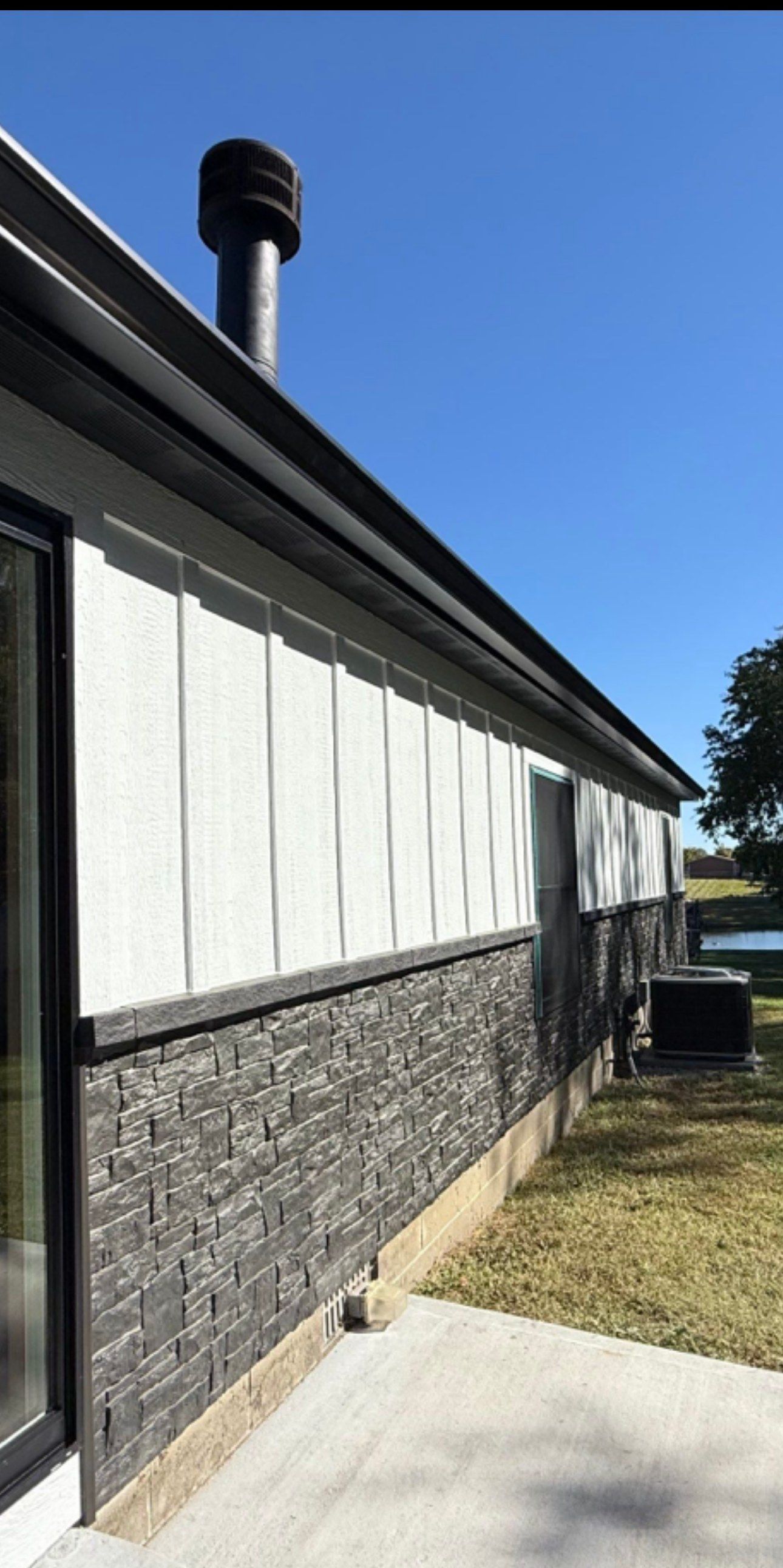 Side wall finished in white board and batten siding over charcoal stone, with a black sliding door