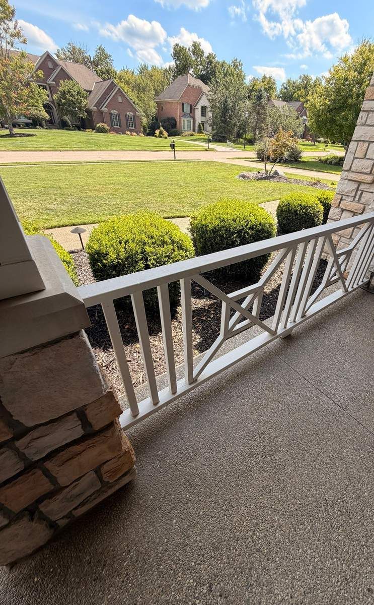 White porch railing with diagonal accents on a stone-column front porch, part of a Fortress Solutions railing repair