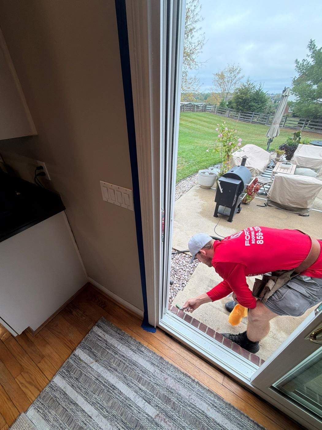 Fortress Solutions crew member applying sealant at the sill of a new white vinyl sliding patio door