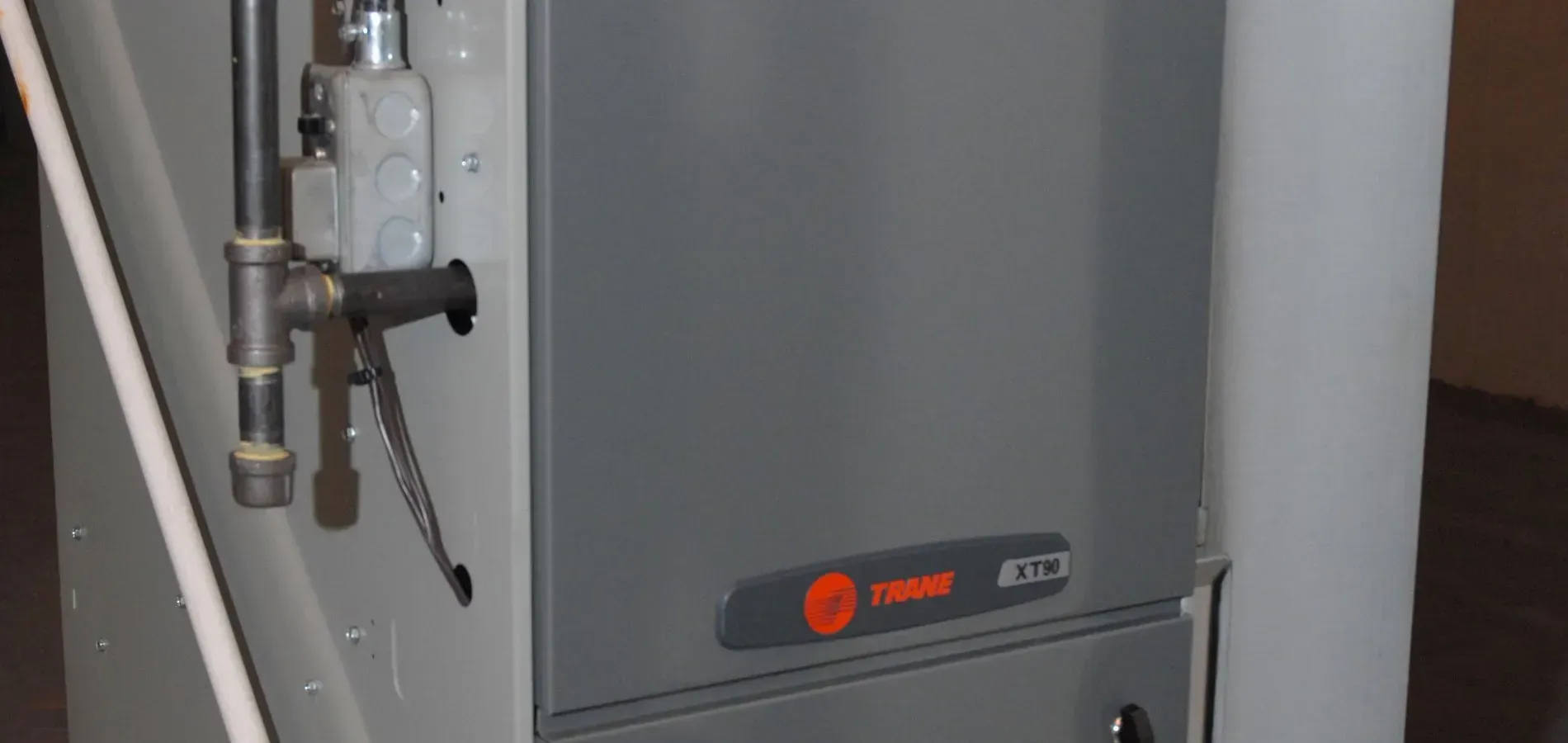 Gray industrial HVAC unit with pipes and a control valve against a wall
