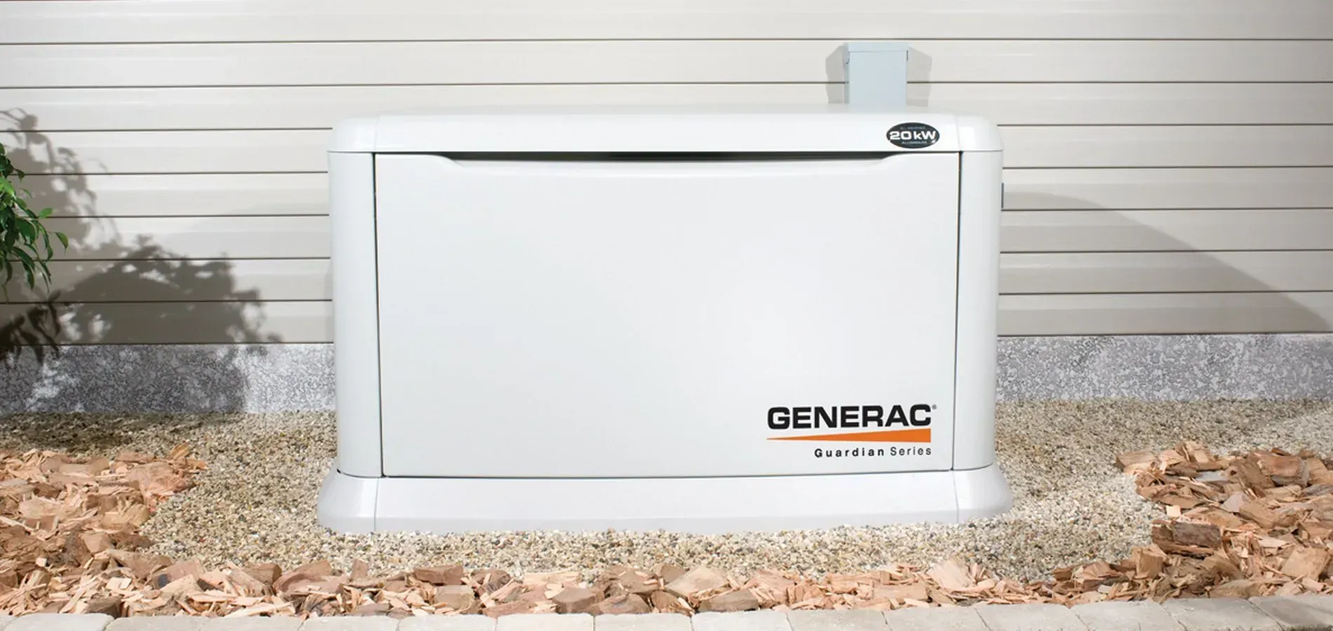 White Generac home generator outdoors against a house wall and gravel bed