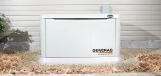 White Generac backup generator outdoors beside a house wall and gravel bed