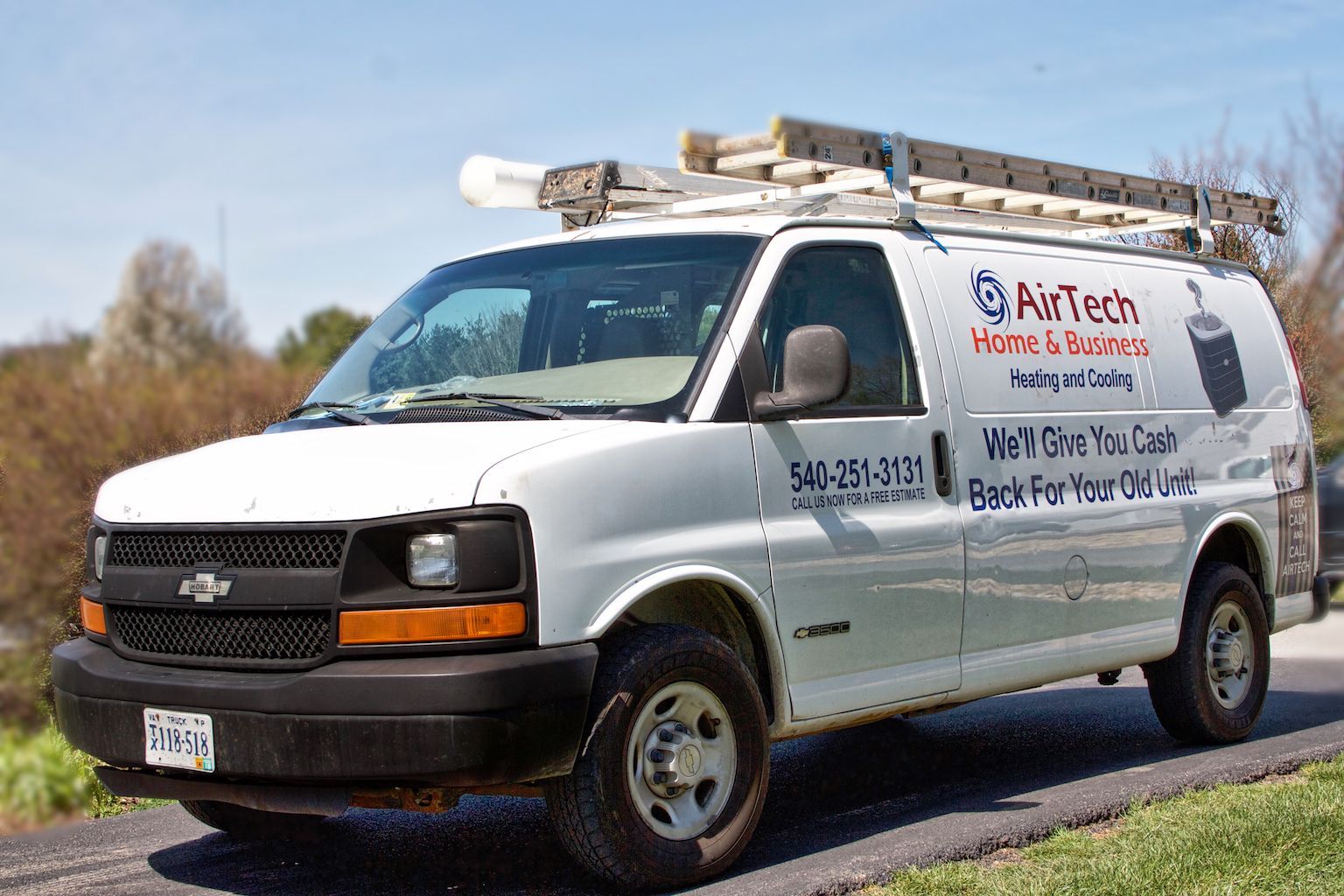 White service van with ladders on top and company logo parked on a roadside under a clear sky