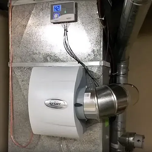 White ventilation unit with digital controller and metal ducting mounted on a basement wall.