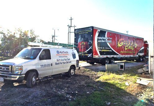 White van and red truck parked in a muddy lot, with a large signboard and debris nearby.