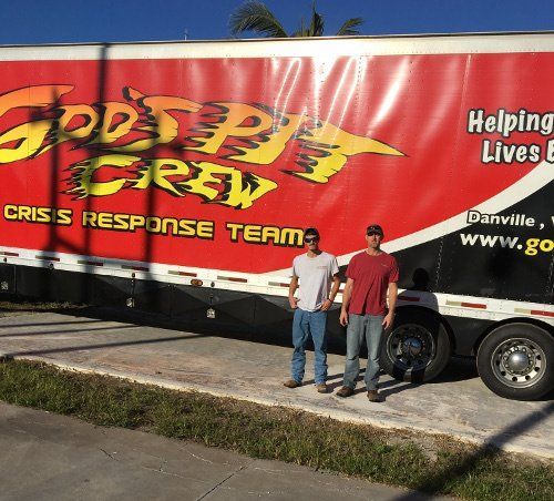 Two people stand beside a red “Disaster Crew” crisis response trailer in a parking lot.